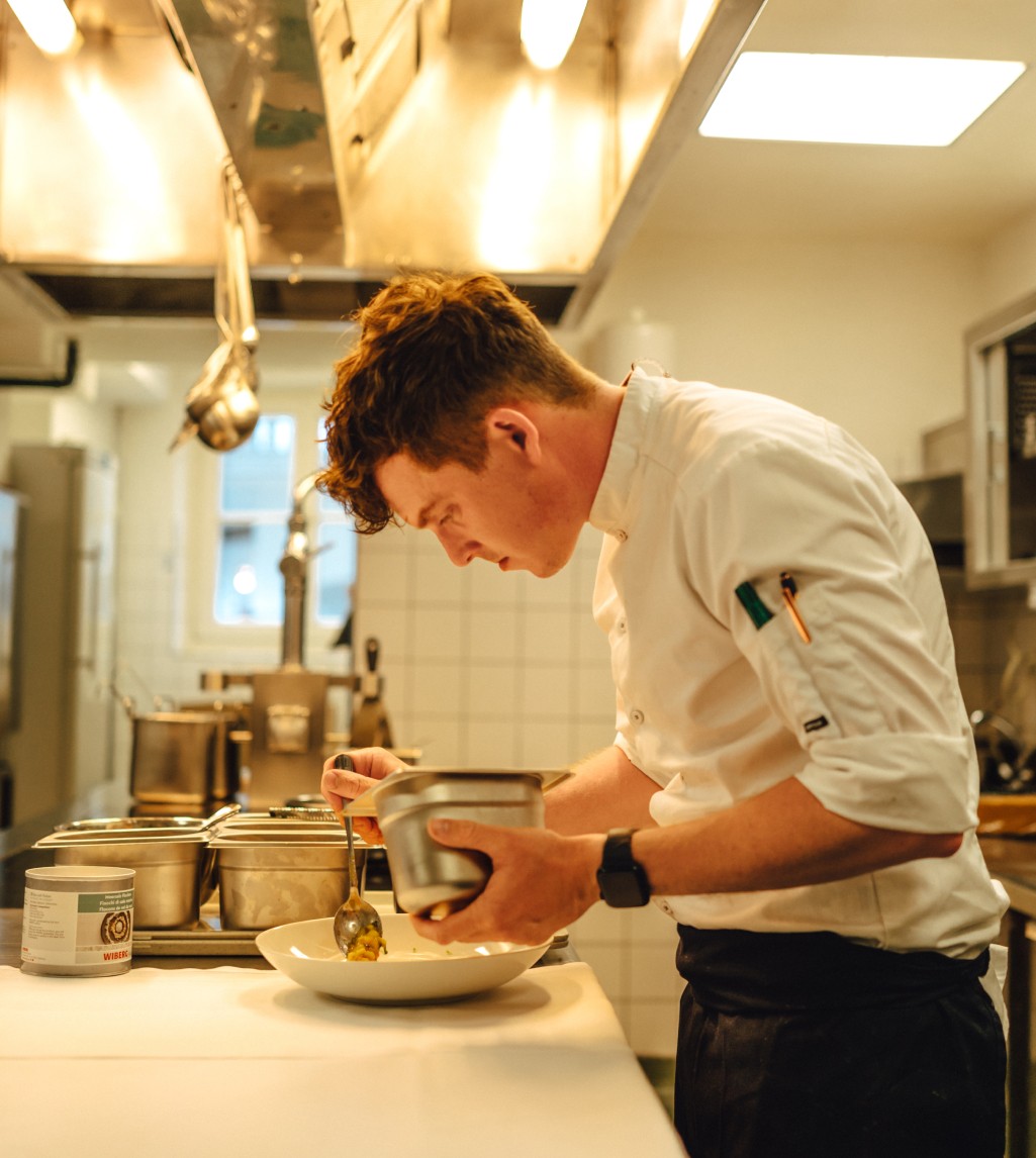 Koch im Boutiquehotel Hubertus bereitet sorgfältig ein Gericht mit frischen Zutaten in der Hotelküche zu